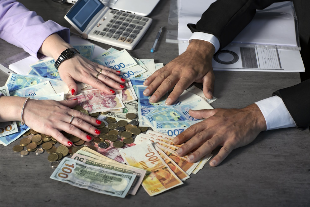 Businessman Hands holding and giving for a contract a fan of money of Israeli New Shekels, GBP and dollars. Cropped image of Hand holds banknotes. Selective focus. A man and a women hands hold a money
